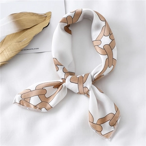Detail view of a white silk scarf with khaki chain pattern tied in a bow on textured fabric