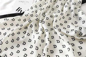 Detailed close-up of a satin silk scarf with letter D patterns and black stitched edges