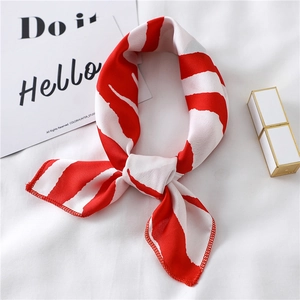 Detailed view of tied red striped silk scarf with gold lipstick on white fabric background