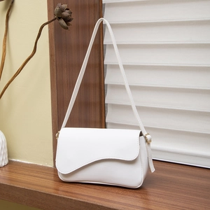 Minimalist white leather underarm bag with gold hardware on a wooden table setup