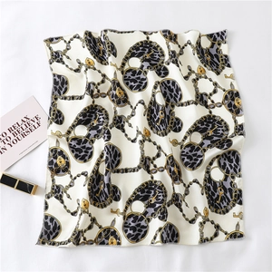 Flat lay of small silk-like scarf with gold chains and leopard heart patterns and lipstick