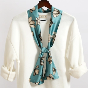 Dettaglio di un foulard in seta floreale verde acqua su un maglione bianco con trama