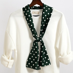 Dettaglio di un foulard di seta verde a pois bianchi annodato su una felpa bianca