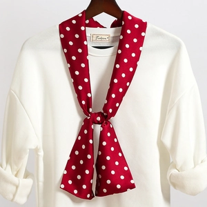 Dettaglio di un foulard di seta rossa a pois bianchi annodato su un maglione bianco