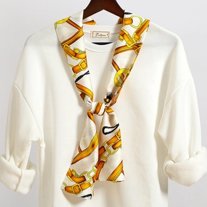 Dettaglio di un foulard in seta con motivi a catena dorata su un top bianco alla moda