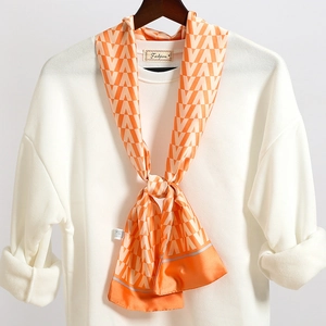 Dettaglio foulard a motivi geometrici arancio e bianco su appendino con maglione bianco