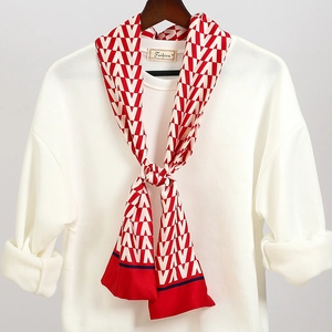 Dettaglio di un foulard in seta geometrico rosso e bianco annodato su una felpa bianca