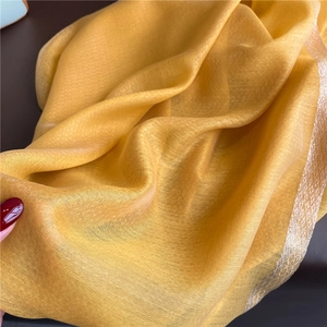 Detailed close-up of yellow silk scarf with elegant gold metallic embroidery edges