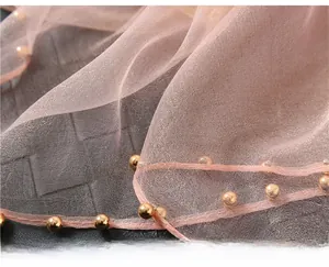Detail of light pink silk wool scarf featuring delicate gold bead trim and woven texture