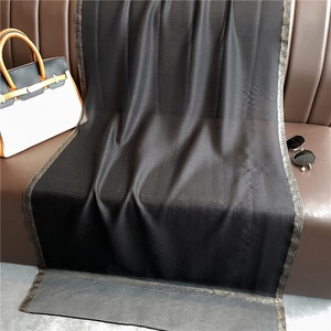 Close-up of black silk-wool scarf with shimmering gold glitter edges on leather surface