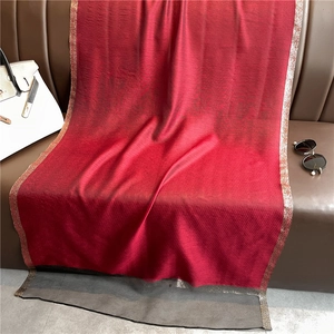 Detail of burgundy silk shawl with golden edges draped on leather furniture