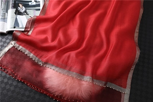 Close-up of vibrant red silk scarf featuring golden metallic trim and tiny bead charms