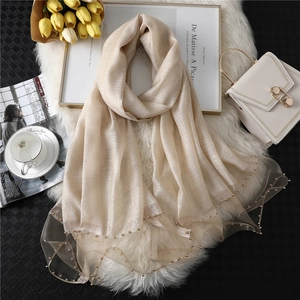 Detail of champagne gold silk scarf featuring elegant beaded mesh edges on plush background