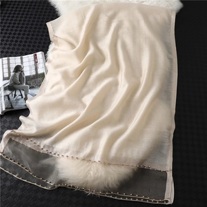 Detail of off-white silk scarf featuring delicate pearl beads on a soft plush background