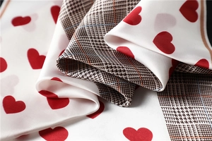 Detailed view of silk-like satin fabric with red hearts and brown houndstooth pattern