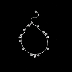 Macro detail of a silver beaded necklace with round zircon pendants on a black background