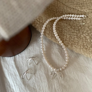 Detail view of pearl necklace and bow earrings set on elegant linen background