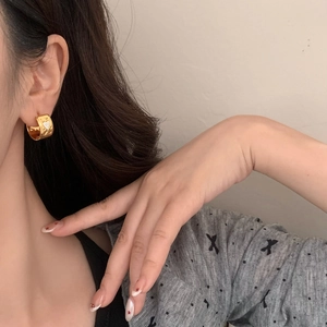 Close-up of golden vintage heart-patterned hoop earring worn by a model