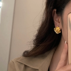 Golden rose stud earrings with layered metallic petals worn in a mirror selfie