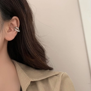 Détail d'un ear cuff croisé argenté serti de zircons porté sur l'oreille du mannequin