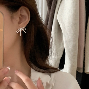 Elegant silver bow stud earrings with a delicate wire design worn by a model