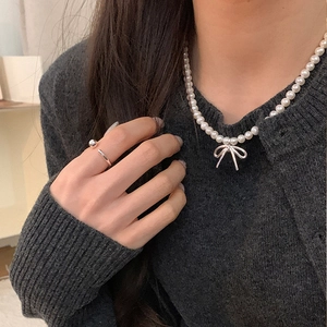 Close-up of pearl necklace with bow pendant and silver minimalist open ring on model