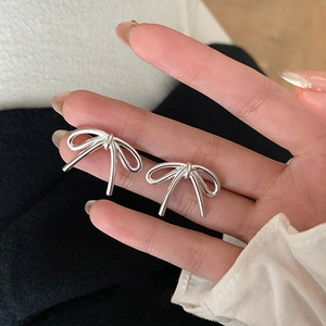 Close-up of minimalist silver bow stud earrings held between fingers for size reference