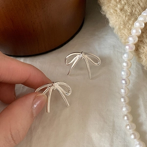 Minimalist silver bow-shaped stud earrings displayed on a rustic fabric background
