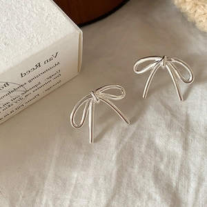 Minimalist silver bow knot earrings with a polished metallic finish on white fabric
