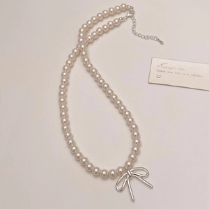 Detail of a pearl necklace featuring a silver bow pendant and adjustable lobster clasp