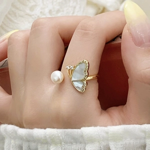 Detailed close-up of adjustable butterfly ring with pearl and shell inlay on finger