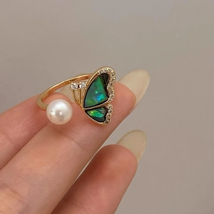 Detailed view of adjustable gold butterfly ring with shell inlay and pearl on finger