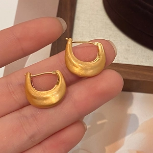 Detailed shot of matte gold U-shaped earrings with a brushed finish texture on fingers
