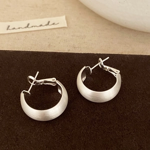 Macro detail of silver brushed matte C-shaped earrings on velvet with a handmade tag