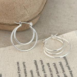 Detailed close-up of triple-layered silver hoop earrings on a neutral linen background