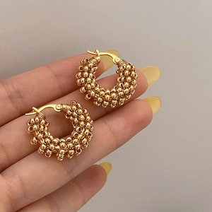 Macro shot of gold hoop earrings with textured bead layers held in hand for scale