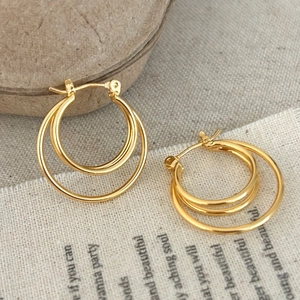 Detailed view of gold triple hoop earrings with a polished finish on natural fabric