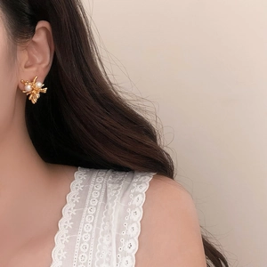 Close-up of golden branch stud earrings with white pearls worn by a model in soft lighting