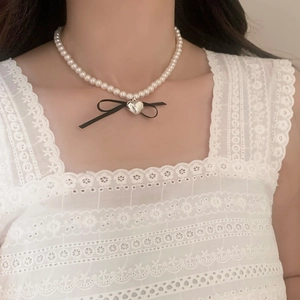 Detail of double-layer pearl necklace featuring a silver heart pendant and black bow