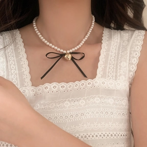 Detail of pearl necklace with a black ribbon bow and golden heart pendant for women