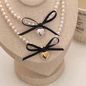 Detail of double-layer pearl necklace with black ribbon bow and polished heart pendant