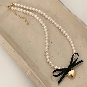 Close-up of pearl necklace with a black satin bow and a gold heart pendant charm