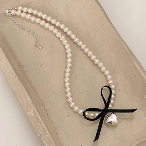 Detailed shot of pearl necklace with a black ribbon bow and silver heart pendant