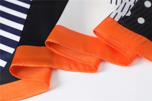 Detail of silk-like scarf with orange trim, blue stripes, and geometric polka dot patterns