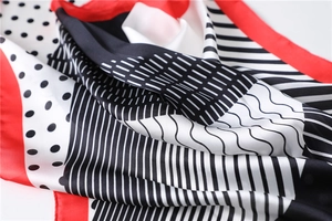 Detailed view of silk-like scarf featuring polka dots, stripes, and red border accents