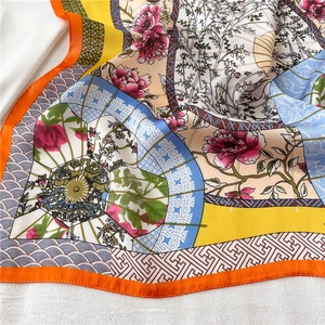 Close-up of a 70cm satin silk scarf featuring vibrant floral prints and orange borders