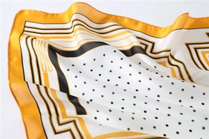 Detail of yellow and black polka dot silk scarf showing satin texture and rolled hem