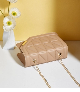 Detail view of beige quilted handbag with gold chain strap and metallic magnetic lock