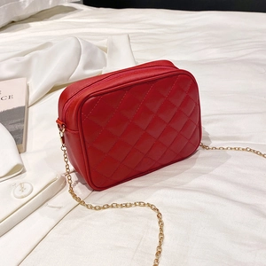 Red quilted faux leather crossbody camera bag with golden chain strap on white bed