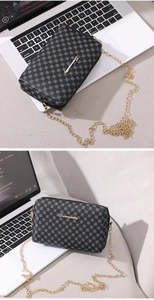 Détail de motifs vintage et logo doré sur petit sac à bandoulière noir avec chaîne